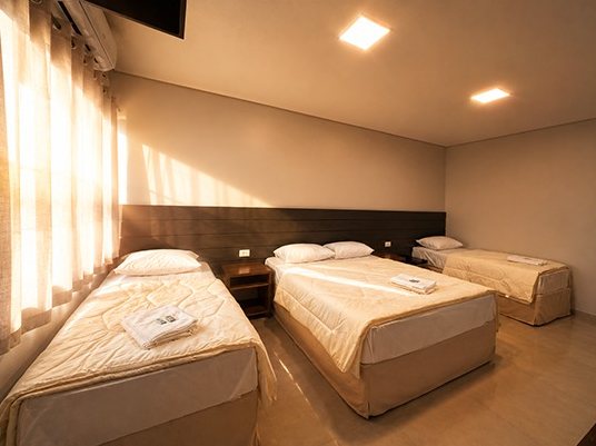 Quarto com três camas de solteiro, cortinas claras e ar-condicionado